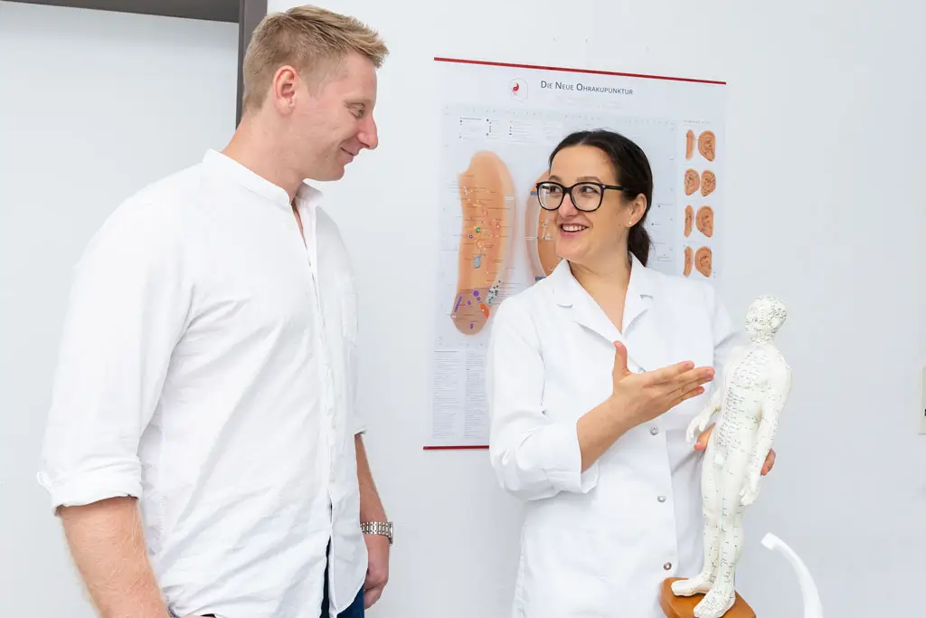 Zahnärztin spricht mit Patient Zahnärztin erklärt einem Patient ein Akupunkturmodell