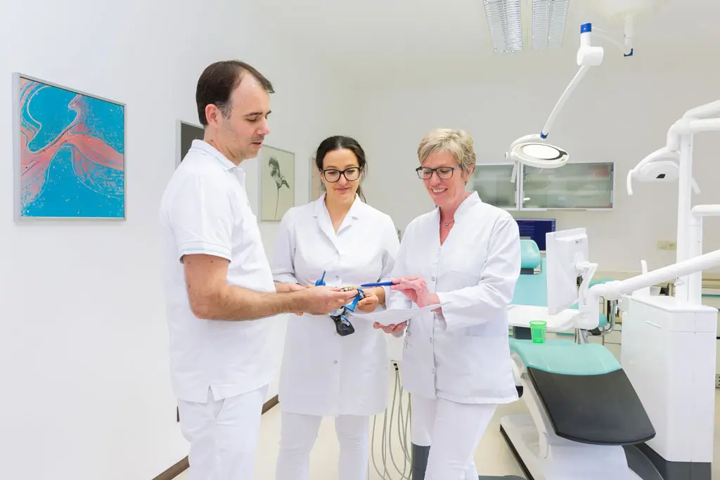 zwei Zahnärztinnen und ein Zahnarzt in weißer Berufskleidung stehen in einer Praxis und besprechen ein Zahnmodell