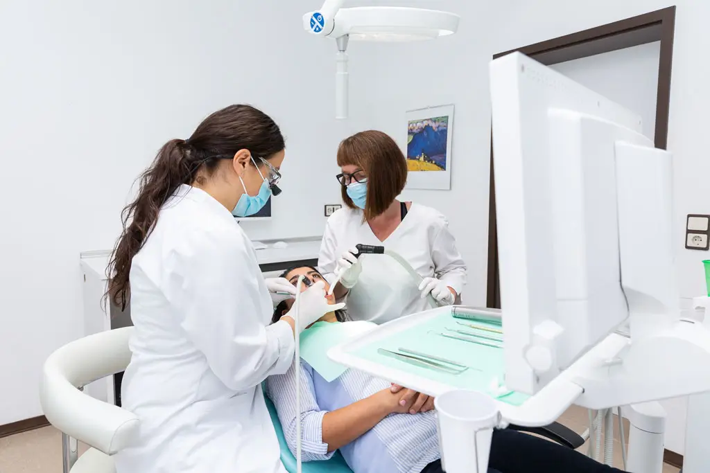 Wurzelkanalbehandlung Zahnärztin und Assistentin führen Wurzelkanalbehandlung bei Patientin im Behandlungsstuhl durch