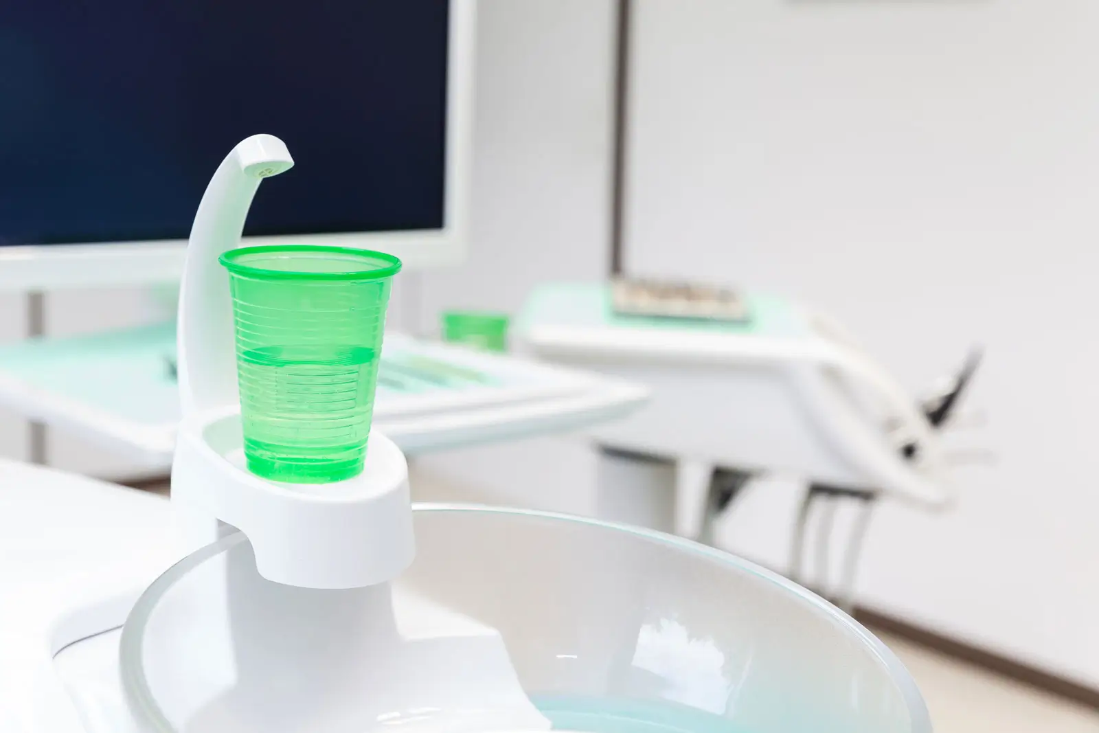 Grüner Plastikbecher auf einem weißen Wasserspender im Behandlungszimmer einer Zahnarztpraxis