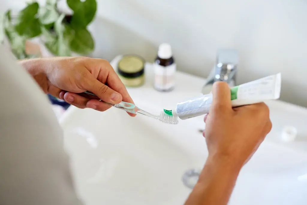 Zahncreme auf Zahnbürste Person drückt Zahnpasta aus einer Tube auf eine Zahnbürste über einem Waschbecken